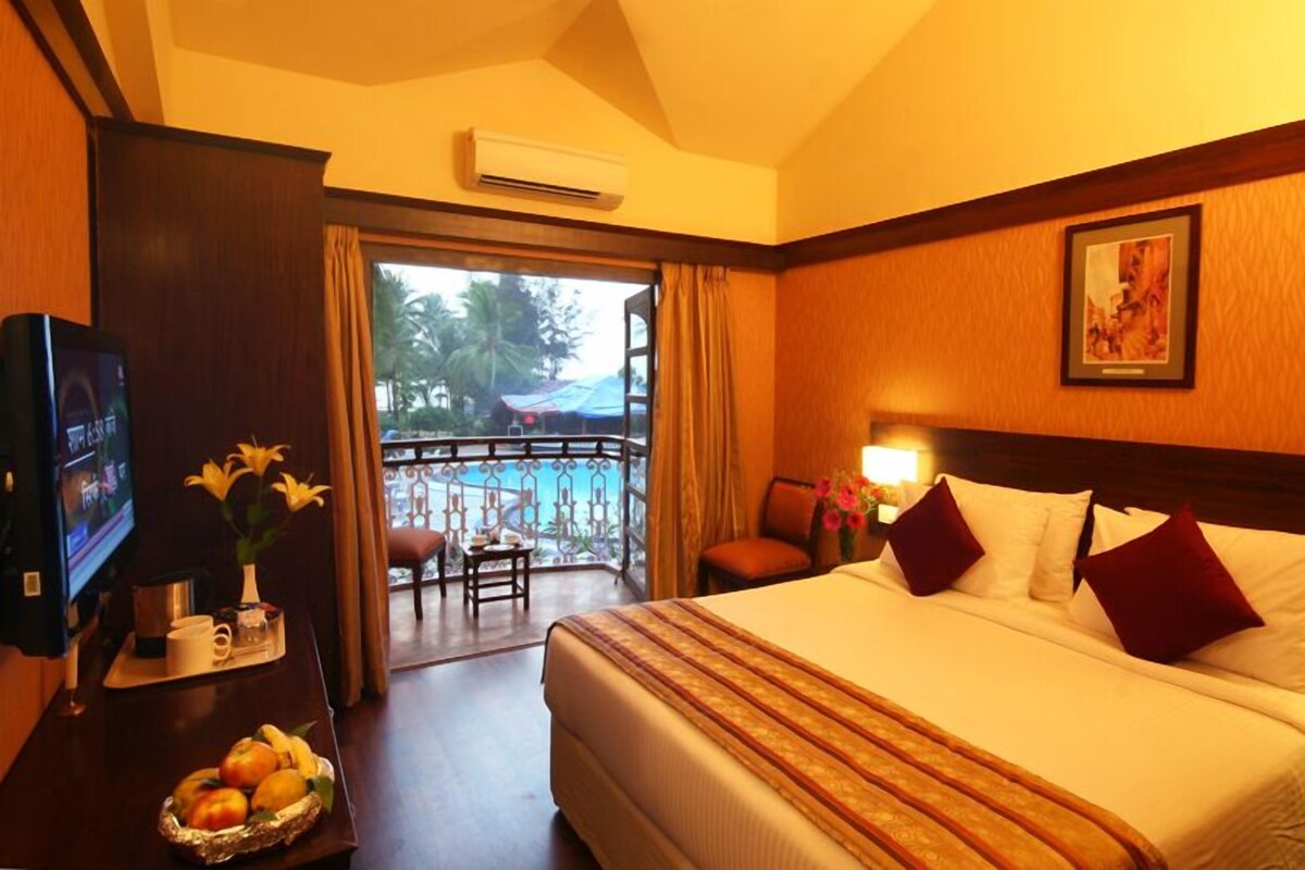 Ein Hotelzimmer mit einem großen Bett, einem Fernseher, einem Balkon mit Blick auf den Pool und einem Essbereich mit Obst.