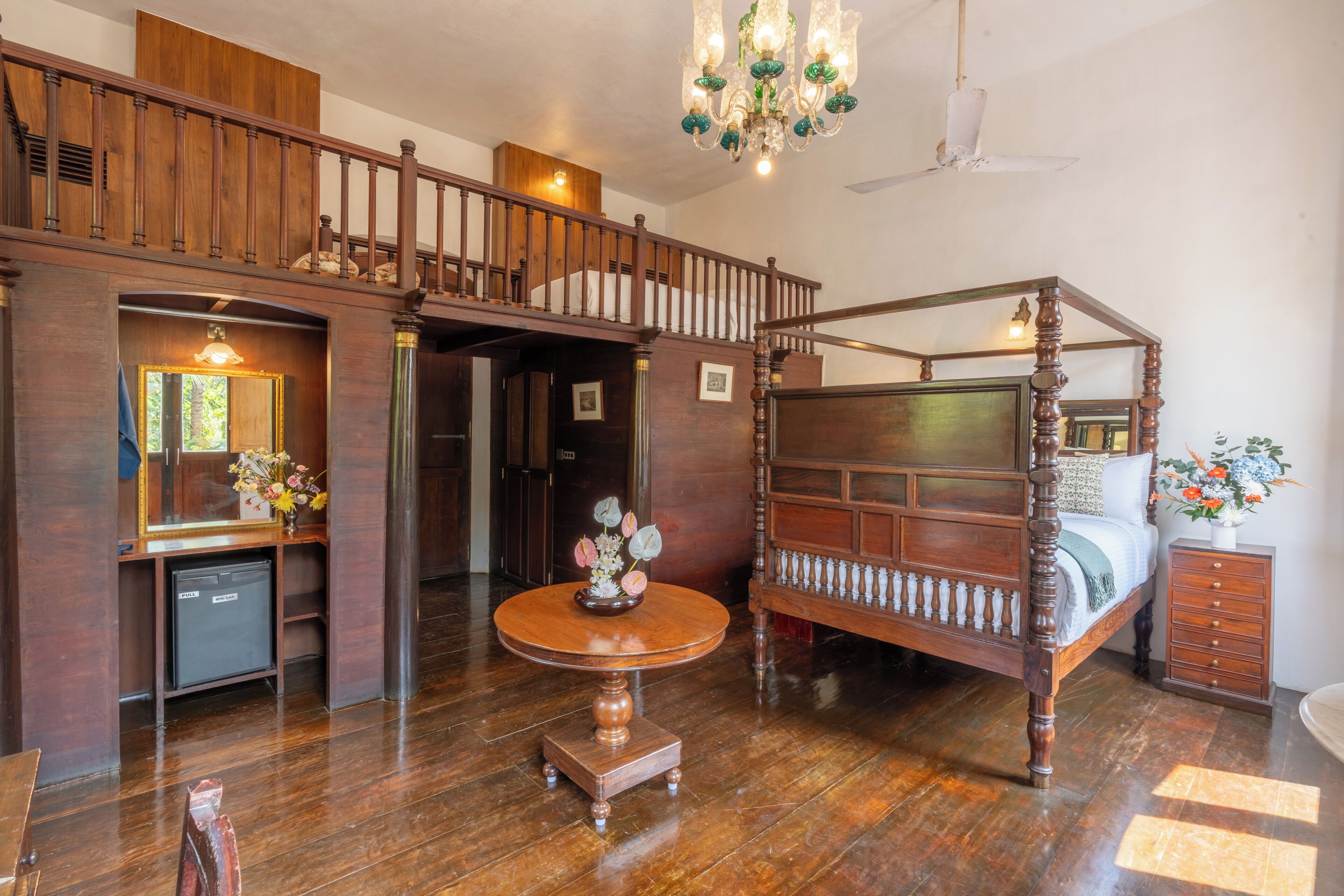 Un lit à baldaquin, un bureau en bois avec un miroir et un lustre dans une pièce dotée d’un plancher en bois et d’un escalier.