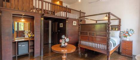 Un lit à baldaquin, un bureau en bois avec un miroir et un lustre dans une pièce dotée d’un plancher en bois et d’un escalier.