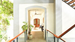 A hallway with a ceiling fan, a potted plant, and a staircase with a wooden handrail. - Le Dupleix (Puducherry)