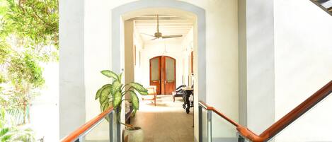 A hallway with a ceiling fan, a potted plant, and a staircase with a wooden handrail.