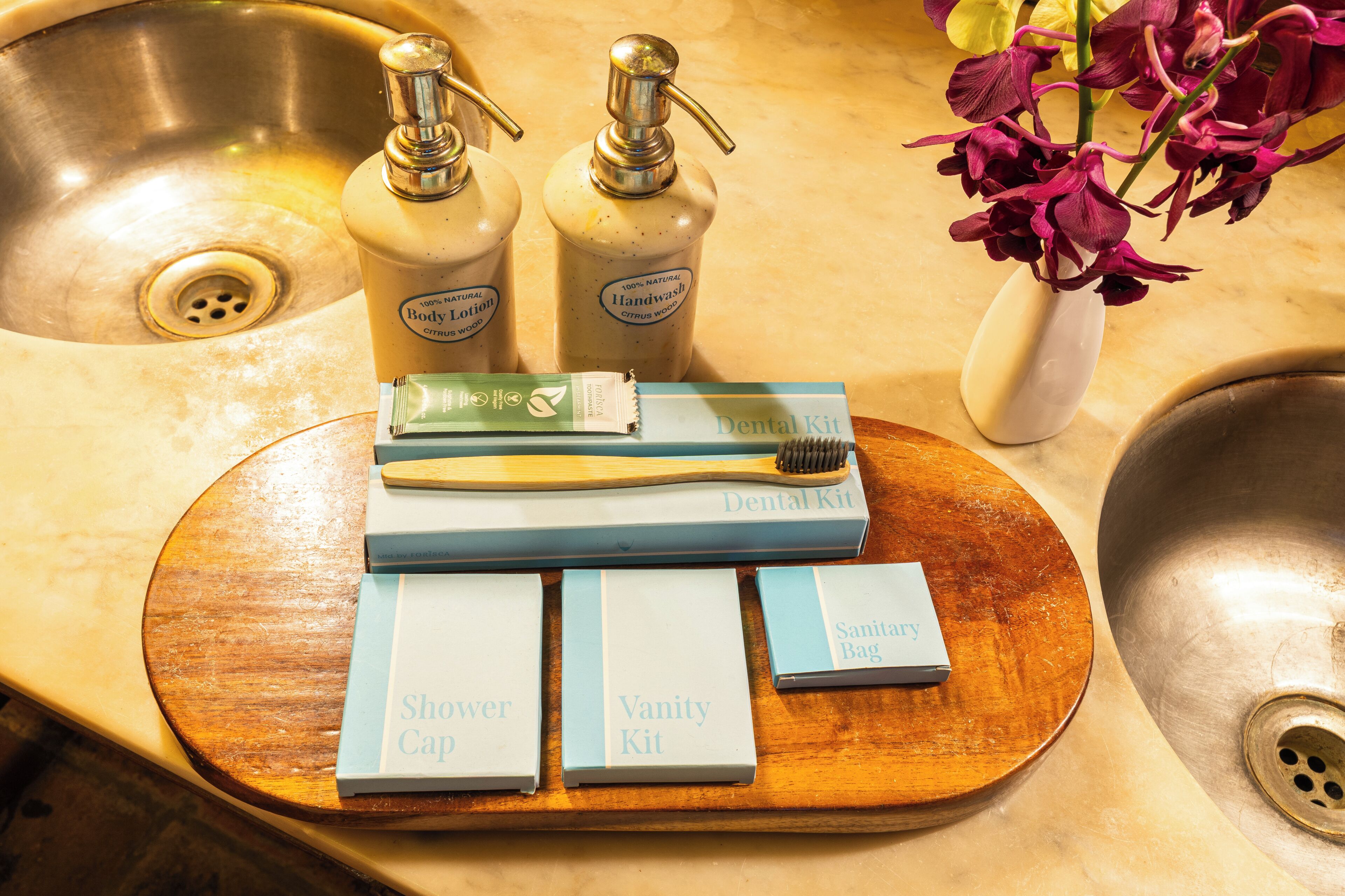 A bathroom sink with two handwash bottles, a toothbrush, a dental kit, a shower cap, a vanity kit, and a sanitary bag.