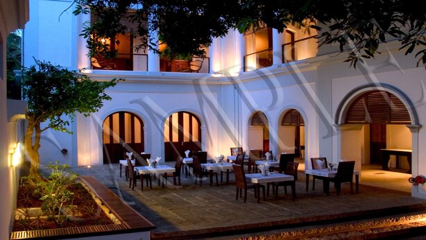 An outdoor dining area with tables and chairs, surrounded by white walls and arches. - Le Dupleix (Puducherry)