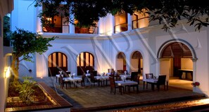 An outdoor dining area with tables and chairs, surrounded by white walls and arches. - Le Dupleix (Puducherry)