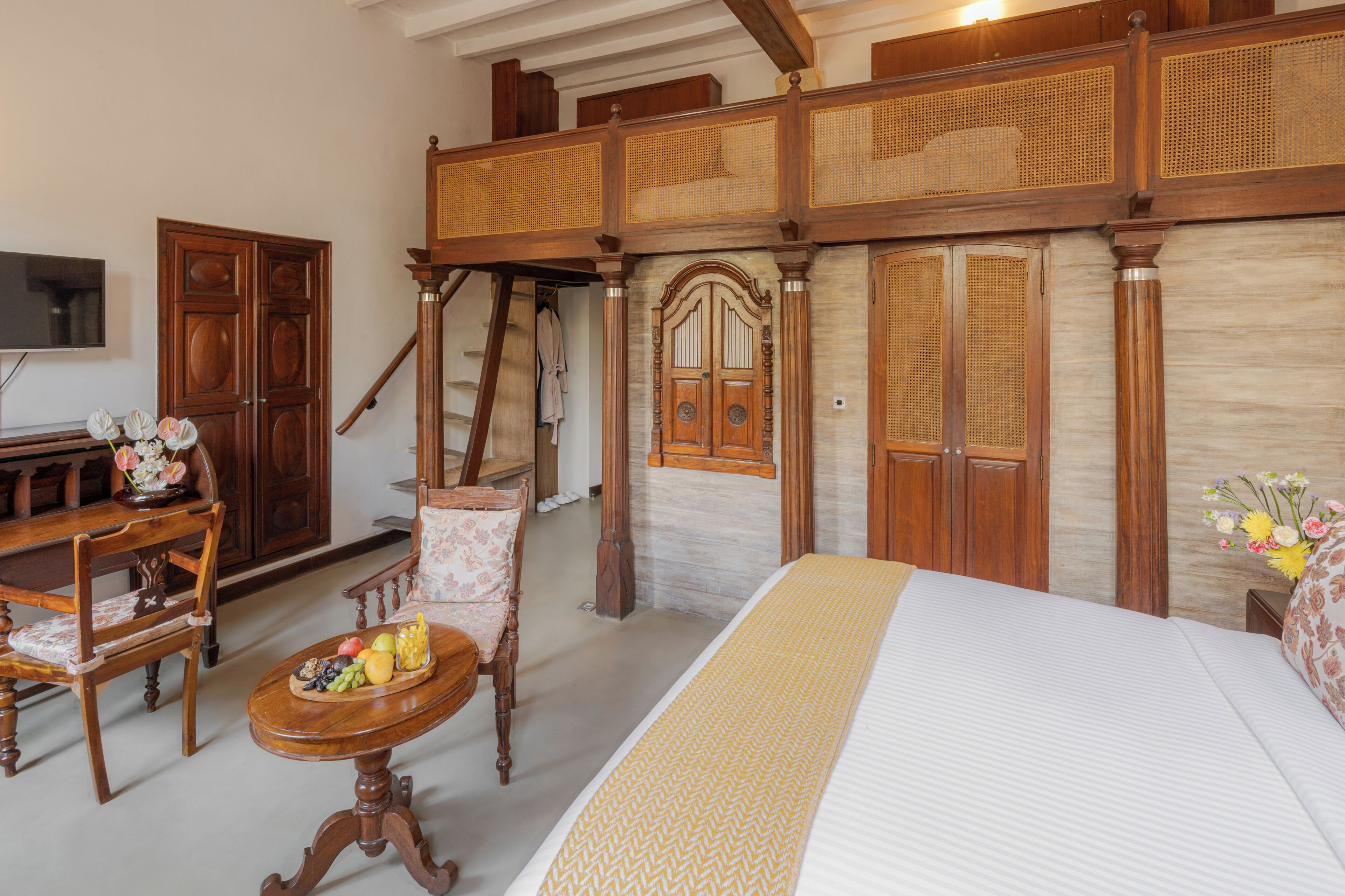 Una stanza con un letto, una scrivania in legno con della frutta, una sedia, un televisore e una scala.