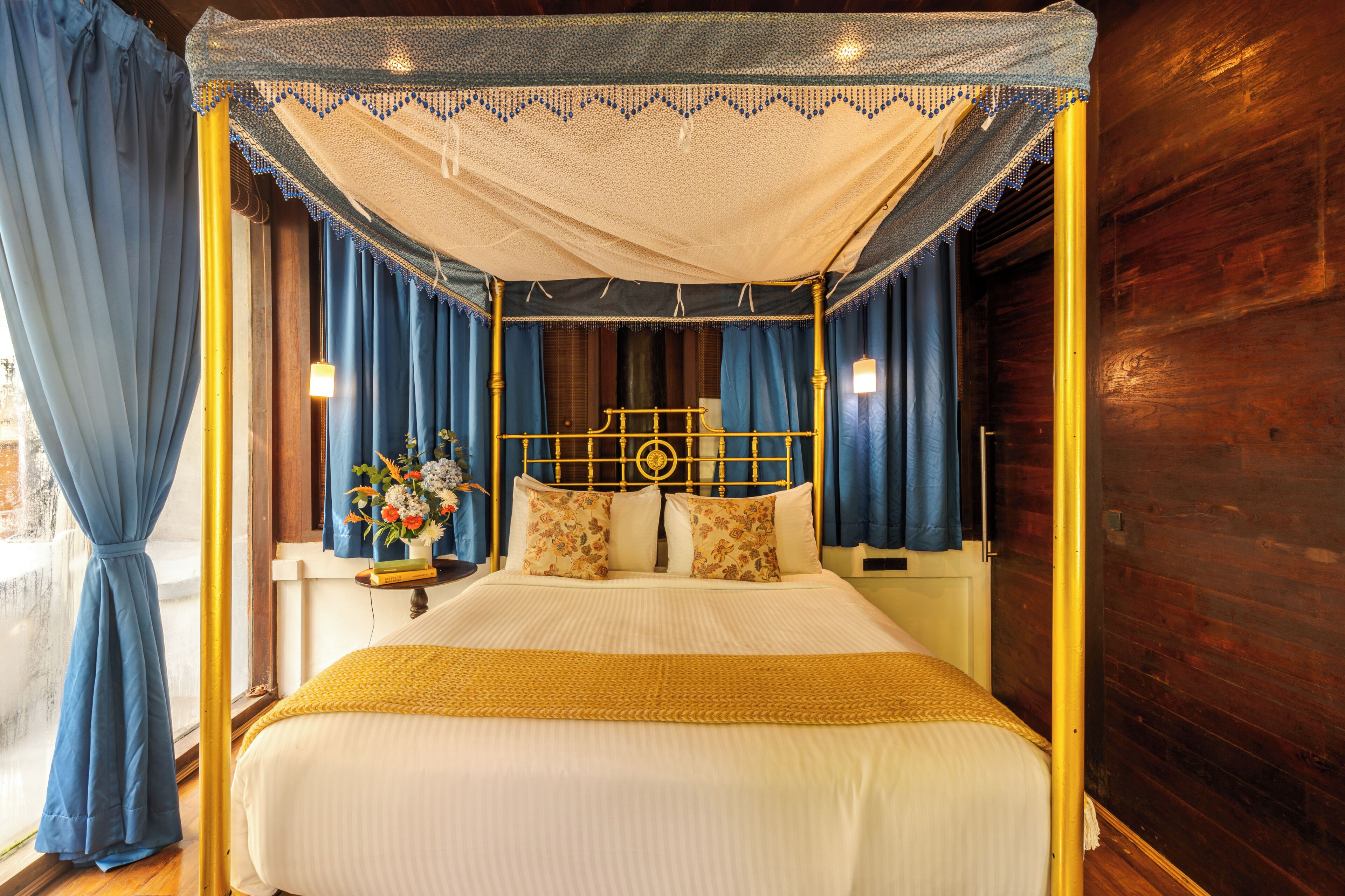 A four-poster bed with a canopy, a nightstand with a lamp, and a vase with flowers.