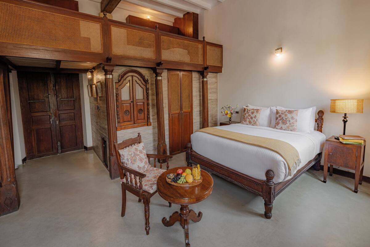 Quarto tradicional com uma cama grande, mobiliário de madeira e uma cesta de frutas em uma mesa de cabeceira.
