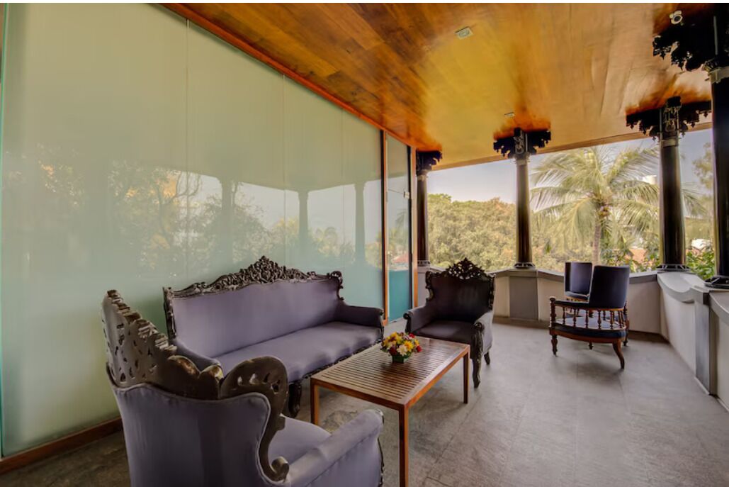 A room with a wooden ceiling, a sofa, armchairs, a table with a vase, and a television.