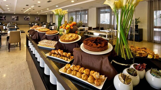 A buffet setup with various desserts and pastries, a buffet line with white plates, and a decorative arrangement with flowers and fruits. - Eurostars Roma Aeterna (Rome)