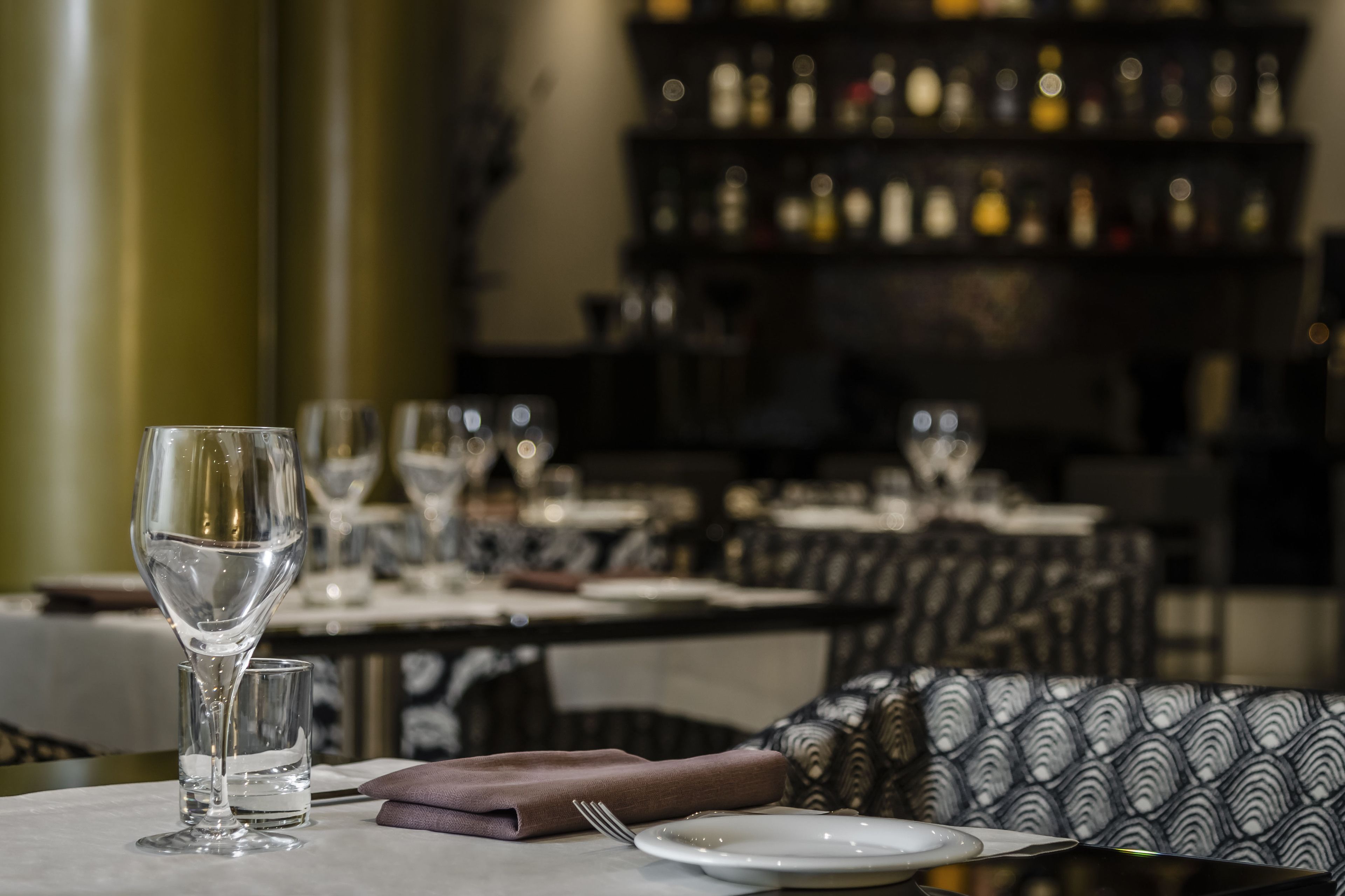 A dining table set with a wine glass, a water glass, a folded napkin, a fork, and a plate.