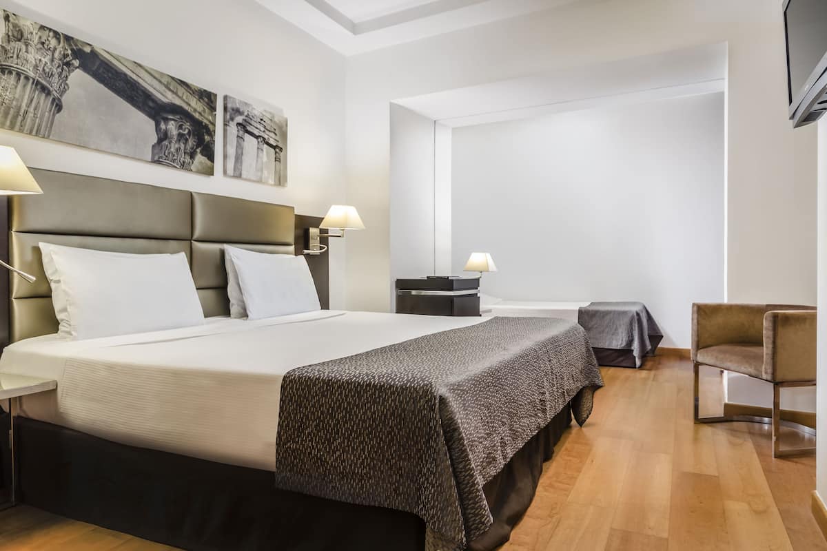 A hotel room with a large bed, two bedside tables with lamps, a chair, and artwork on the wall.