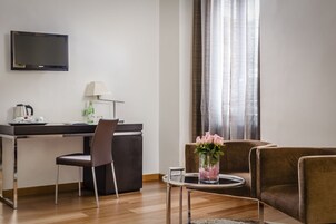 Un soggiorno moderno con una televisione a schermo piatto, una scrivania con una lampada, una macchina per caffè e un vaso con fiori.