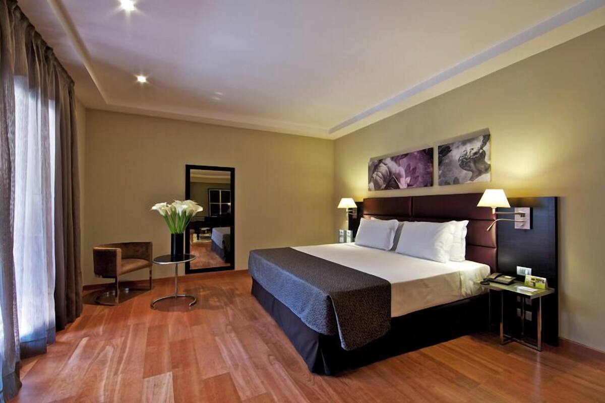 A hotel room with a large bed, two bedside tables, a mirror, and a vase with flowers.