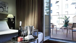 A hotel room with a bed, a bedside table with a tray, a bottle, glasses, and a small gift box. - Eurostars Roma Aeterna (Rome)