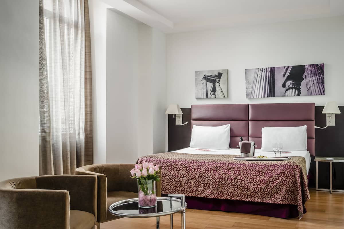 A hotel room with a large bed, two bedside tables, a small round table with a vase of flowers, and a sofa.