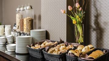 Montaje de bufé con diferentes alimentos, como pan y pasteles, y un florero con flores.