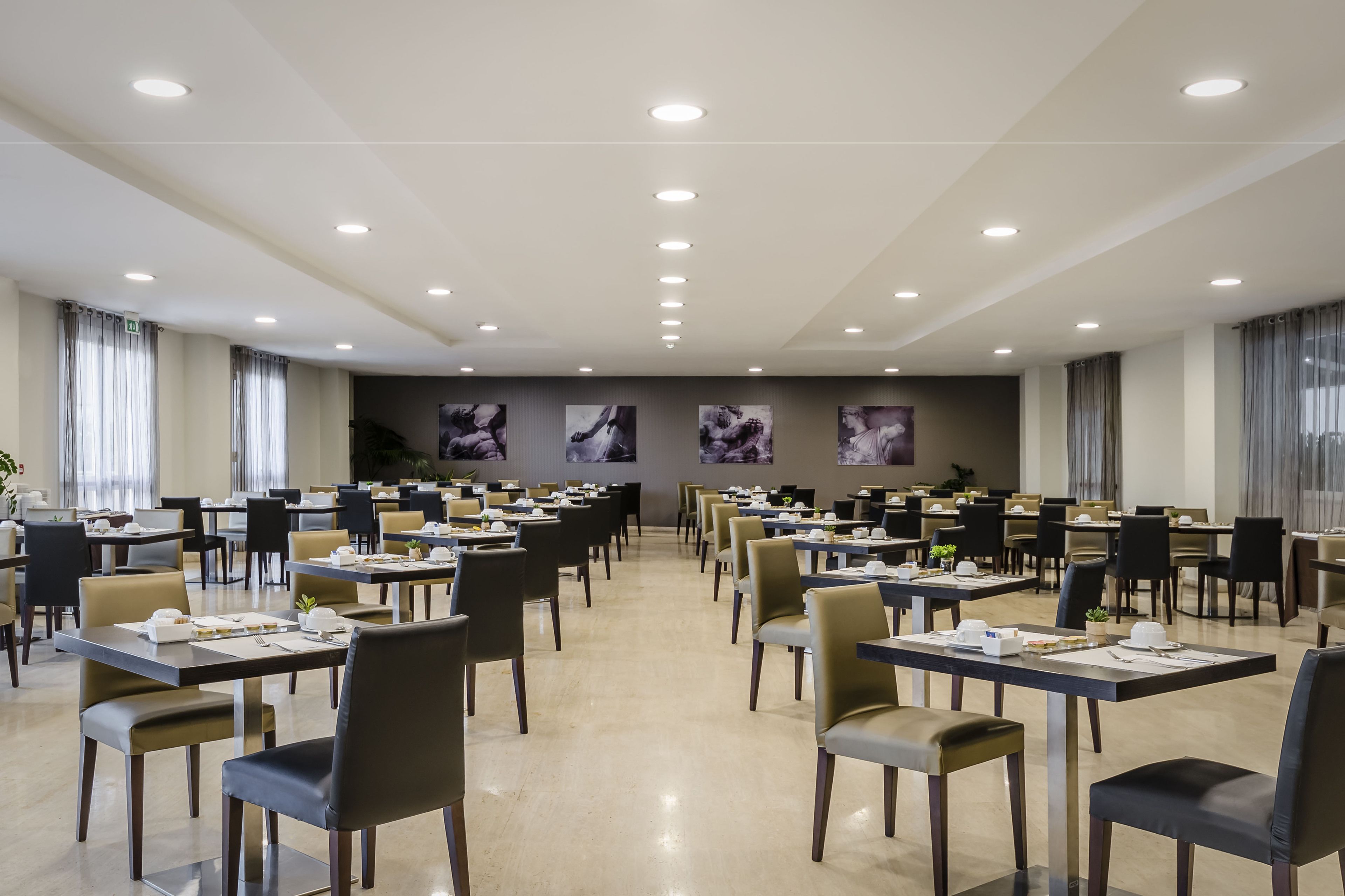 A spacious conference room with multiple tables and chairs, ceiling lights, and framed artwork on the walls.