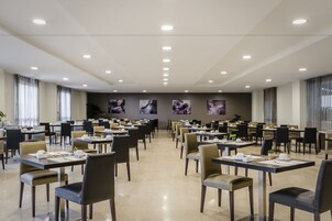 A spacious conference room with multiple tables and chairs, ceiling lights, and framed artwork on the walls.