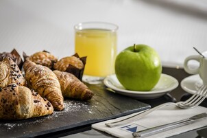 Una colazione con croissant, una mela e un bicchiere di succo d'arancia su un tavolo.
