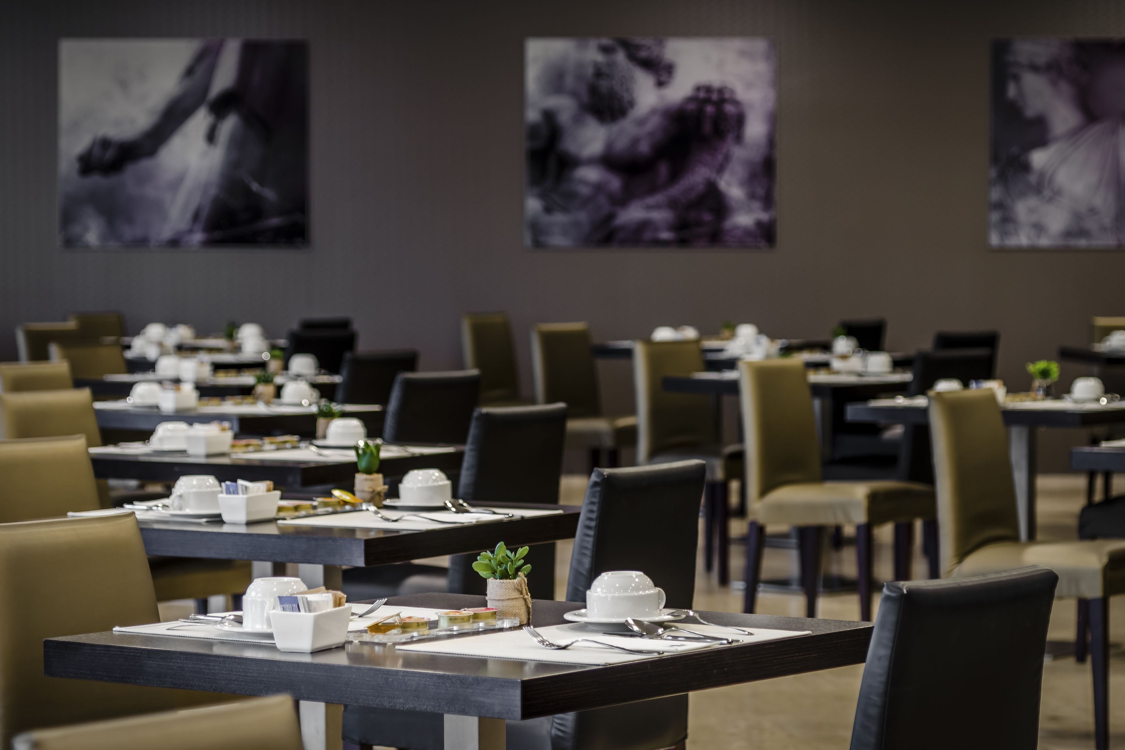 Zona pranzo con tavoli apparecchiati, sedie e opere d'arte alle pareti.