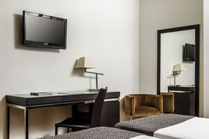 A hotel room with a desk, chair, two beds, a TV, and a mirror.