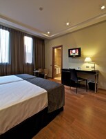 A hotel room with two beds, a desk, a chair, a TV, and a lamp.