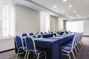 Una sala conferenze con un lungo tavolo, sedie blu e uno schermo per proiezioni.