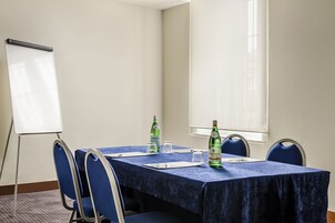 Una sala conferenze con un tavolo blu, sedie, una lavagna e due bottiglie d'acqua.