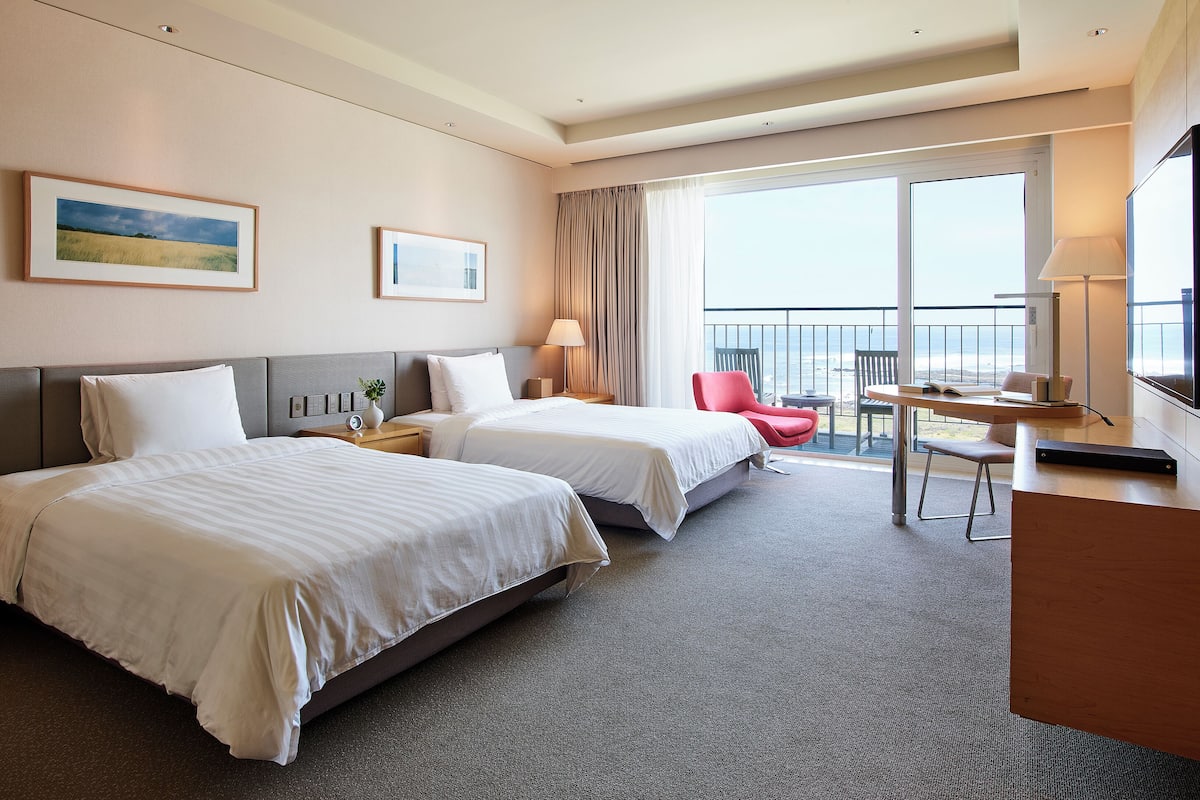 Une chambre d’hôtel avec deux lits, un bureau, une chaise, une télévision et un balcon avec vue.