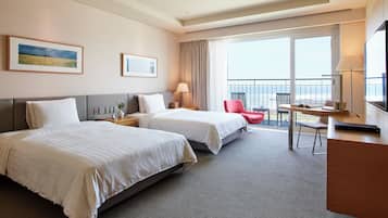 A hotel room with two beds, a desk, a chair, a TV, and a balcony with a view.