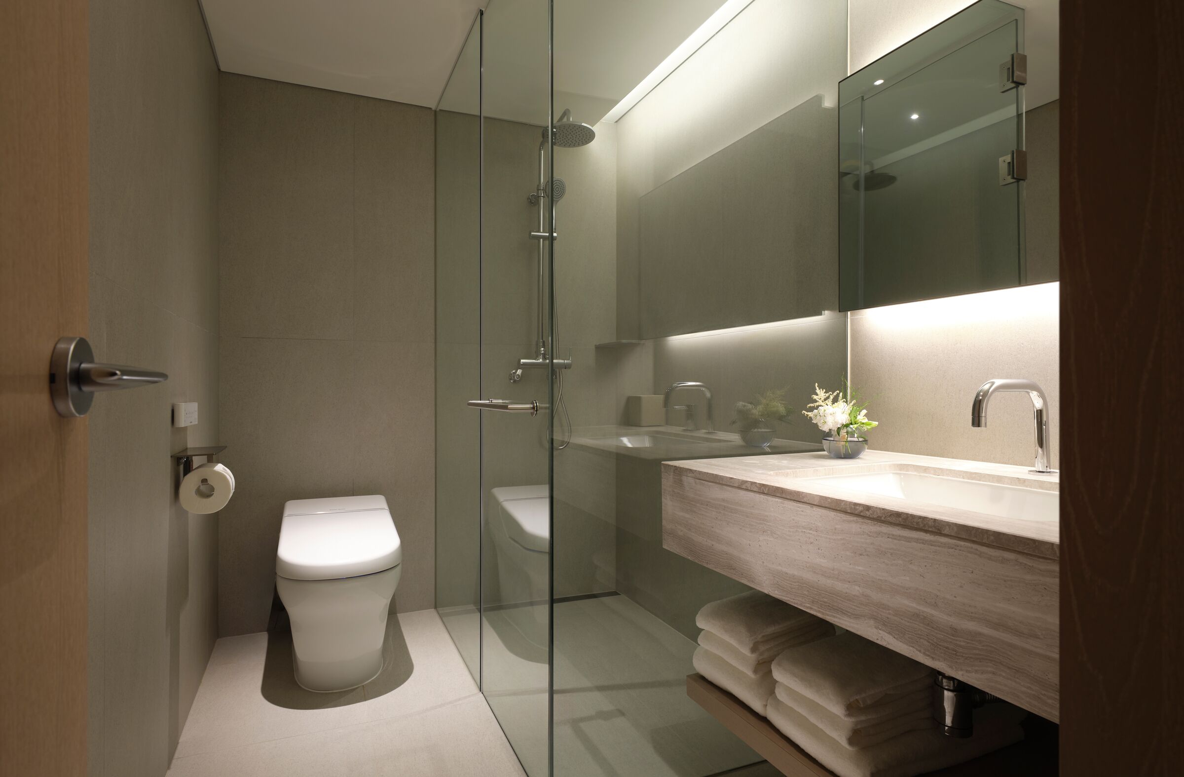 Un baño moderno con ducha envuelta en vidrio, tocador de madera y un espejo grande.