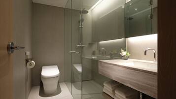 Un baño moderno con ducha envuelta en vidrio, tocador de madera y un espejo grande.