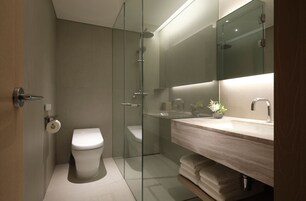 Un baño moderno con ducha envuelta en vidrio, tocador de madera y un espejo grande.