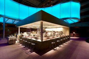 A modern bar area with a central counter, bar stools, and a kitchen visible behind the counter. - Haevichi Hotel and Resort Jeju (Seogwipo)