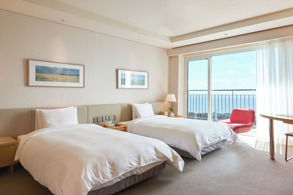 Une chambre d’hôtel avec deux lits, un balcon avec une chaise rouge et une table.