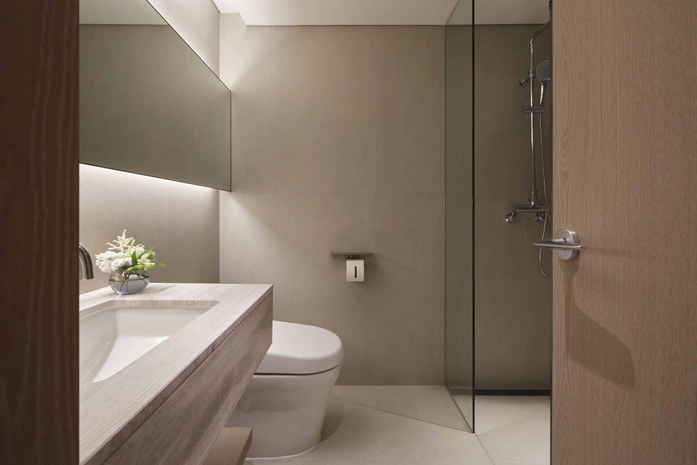 A modern bathroom with a large mirror, a sink, a toilet, and a glass-enclosed shower area.