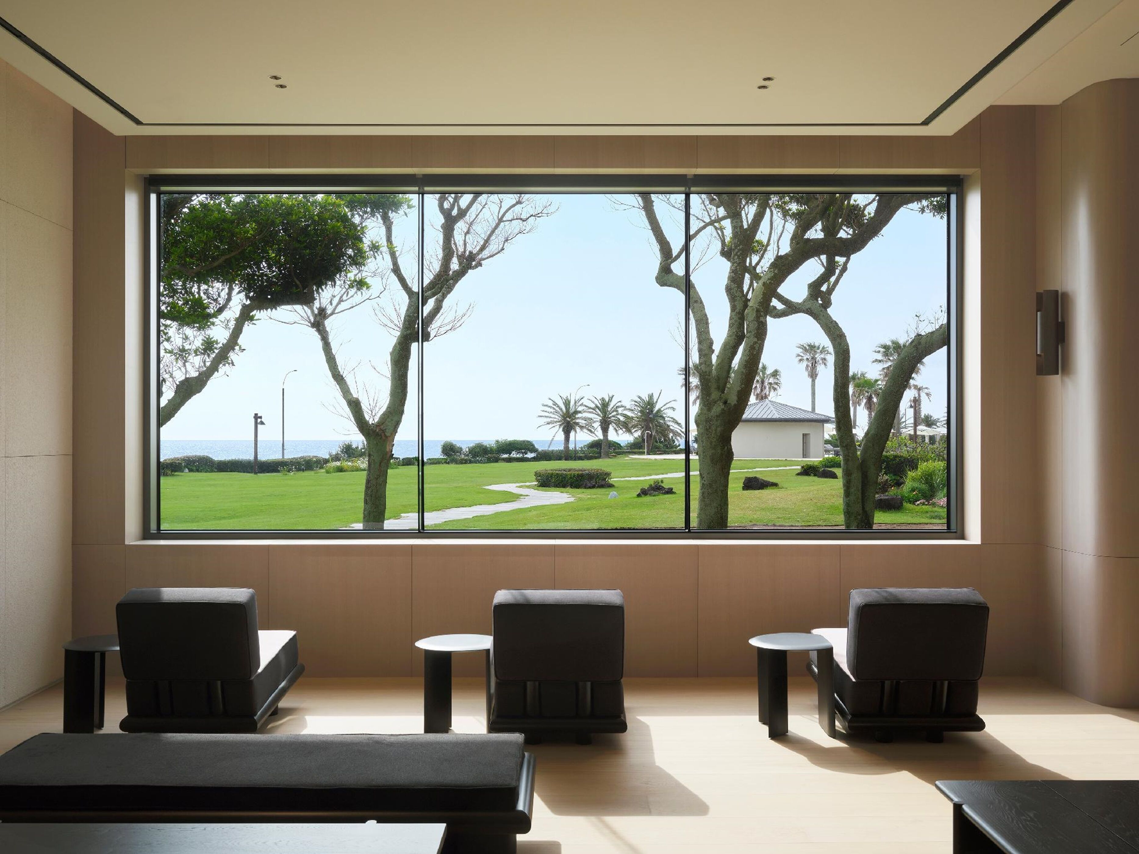 A room with a large window, two chairs, a small table, and a bench.
