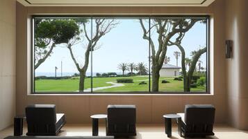 A room with a large window, two chairs, a small table, and a bench.