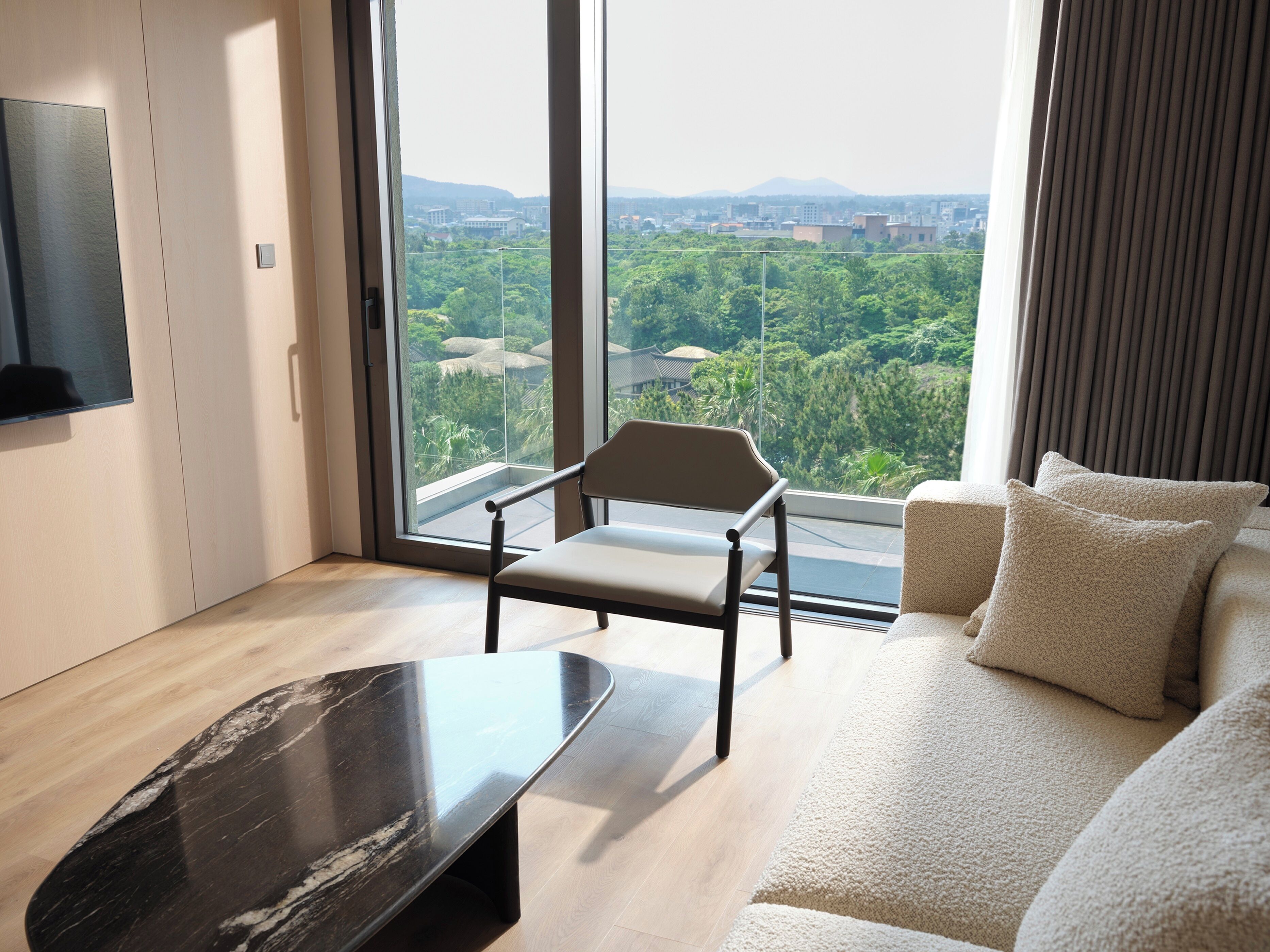 A modern living room with a large window, a sofa, a chair, and a black coffee table.