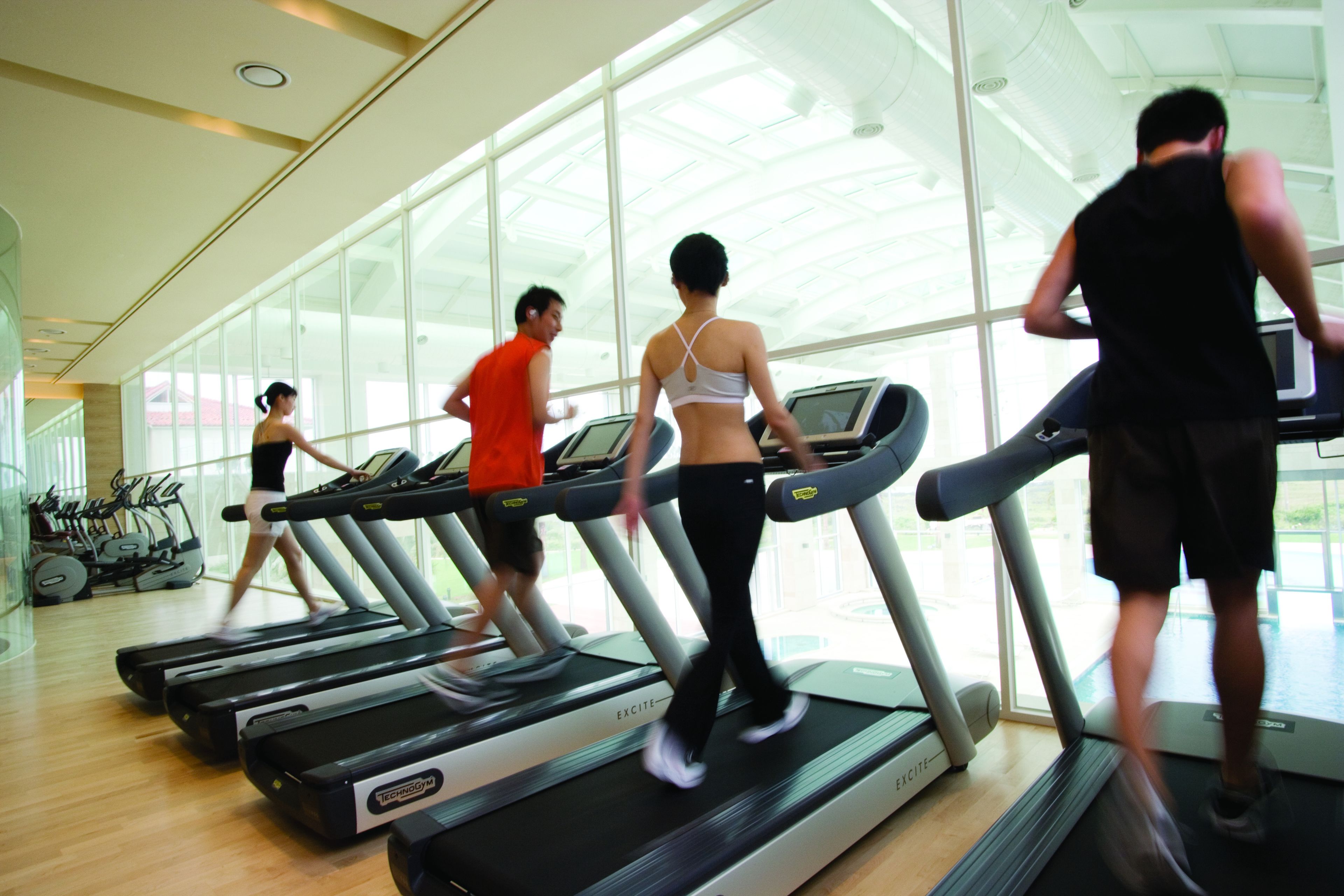 Une salle de sport équipée de tapis de course, de vélos d’exercice et dotée d’un grand mur vitré.