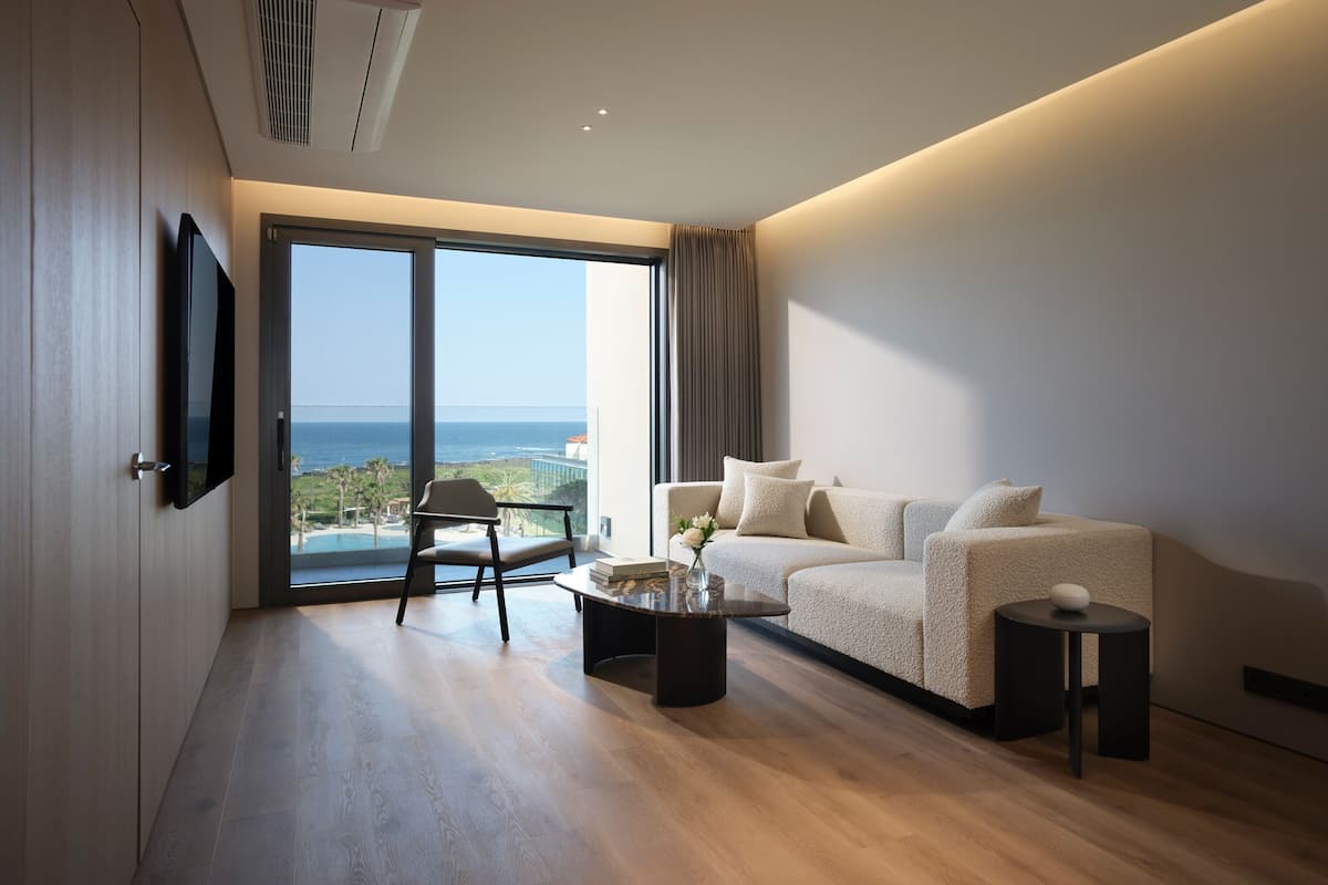 Un salon moderne comprenant un canapé, une table basse, un téléviseur fixé au mur et une grande fenêtre donnant sur l’océan.