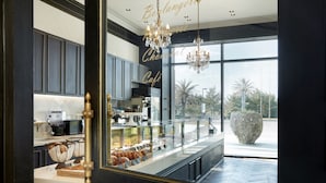 Een modern interieur met een keuken, een cafébalie met gebak en een groot raam met uitzicht op palmbomen.
