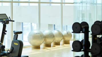 A gym with exercise equipment, large windows, and a wooden floor.
