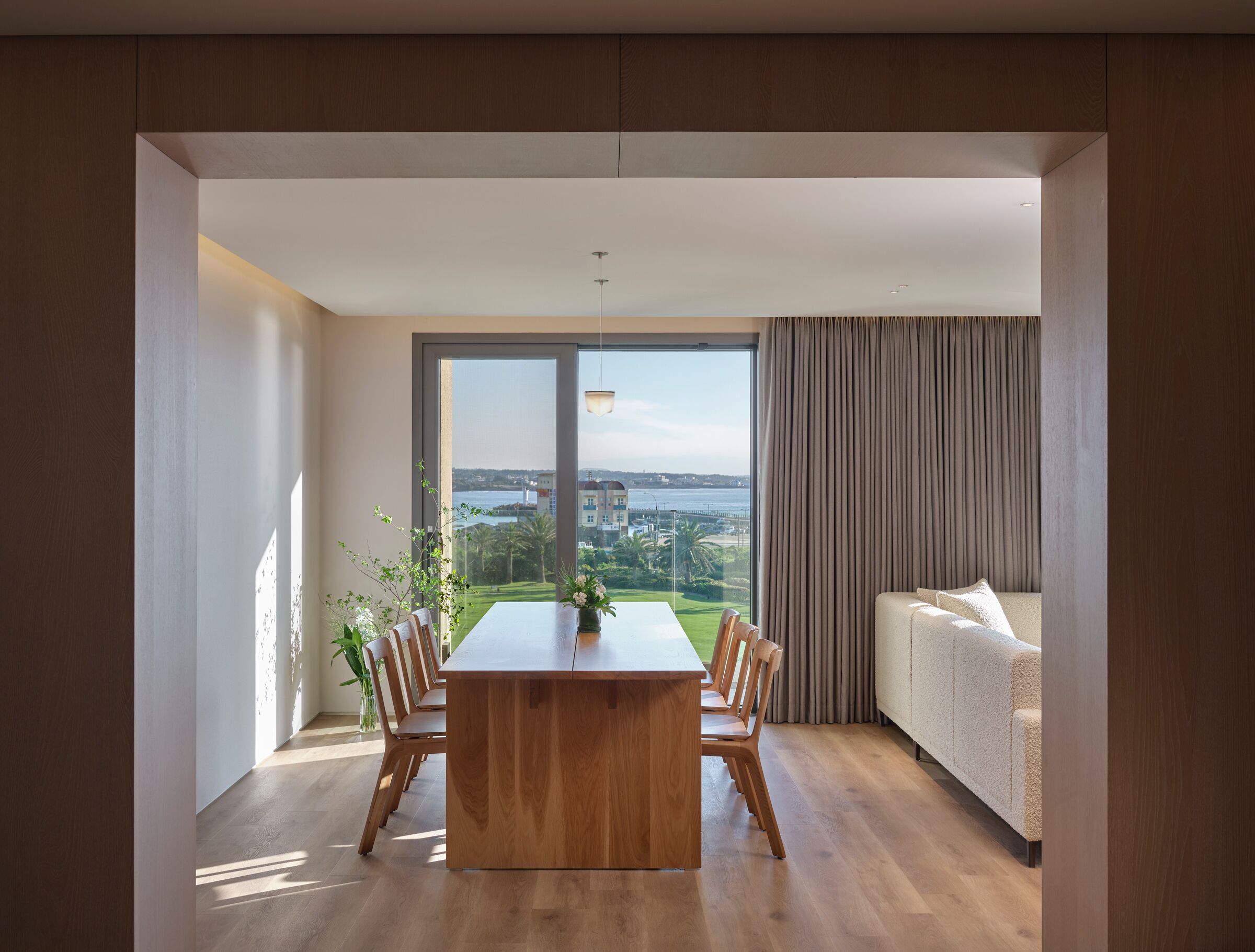 Una sala moderna con un gran ventanal, una mesa de comedor de madera y un sofá.