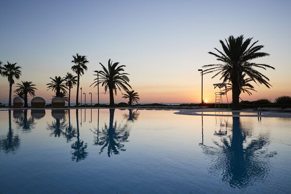 A serene pool area with palm trees and a sunset in the background. - Haevichi Hotel and Resort Jeju (Seogwipo)