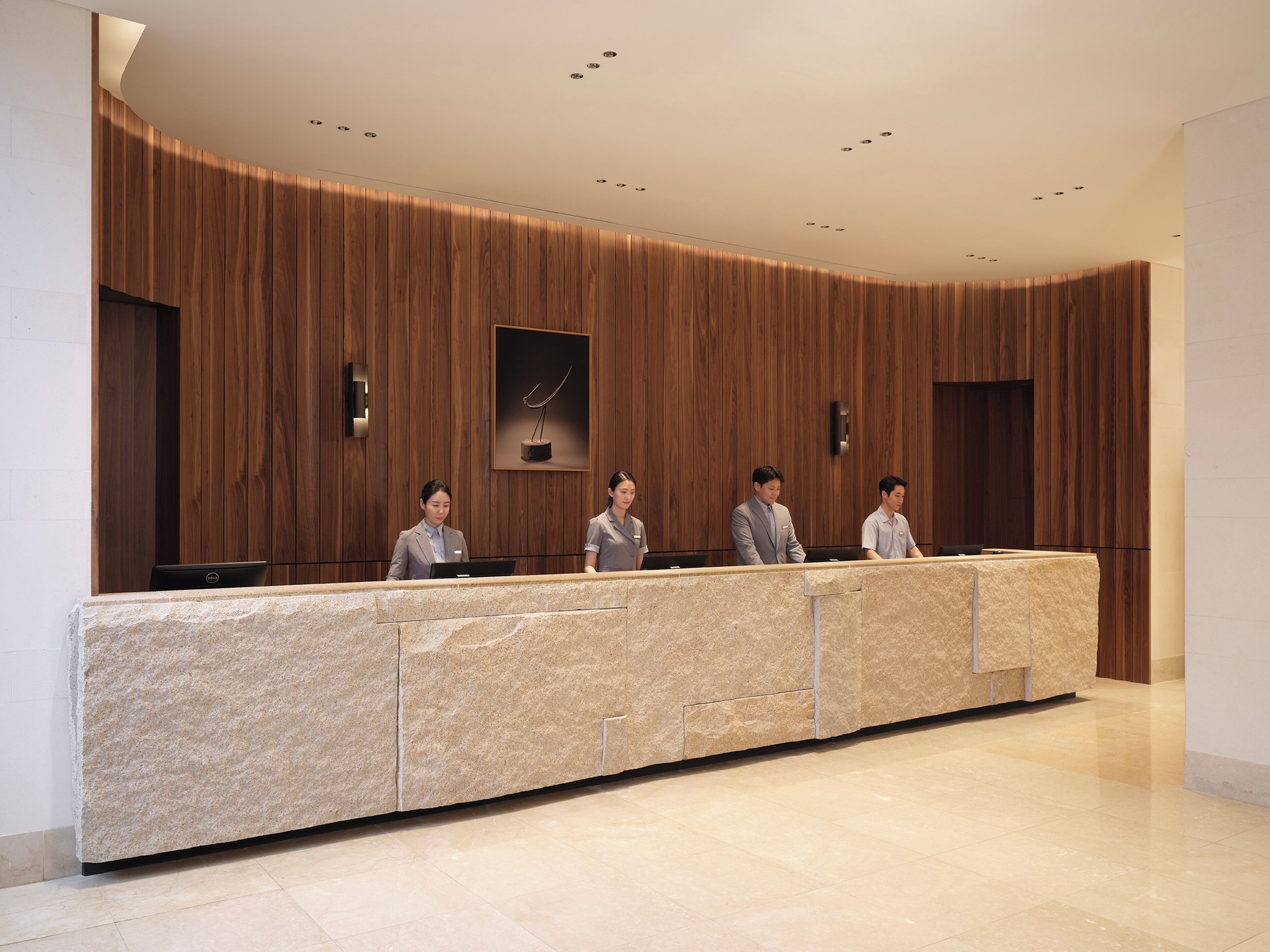 Uma mesa de recepção com bancada de pedra, painéis de madeira nas paredes e uma obra de arte emoldurada acima.
