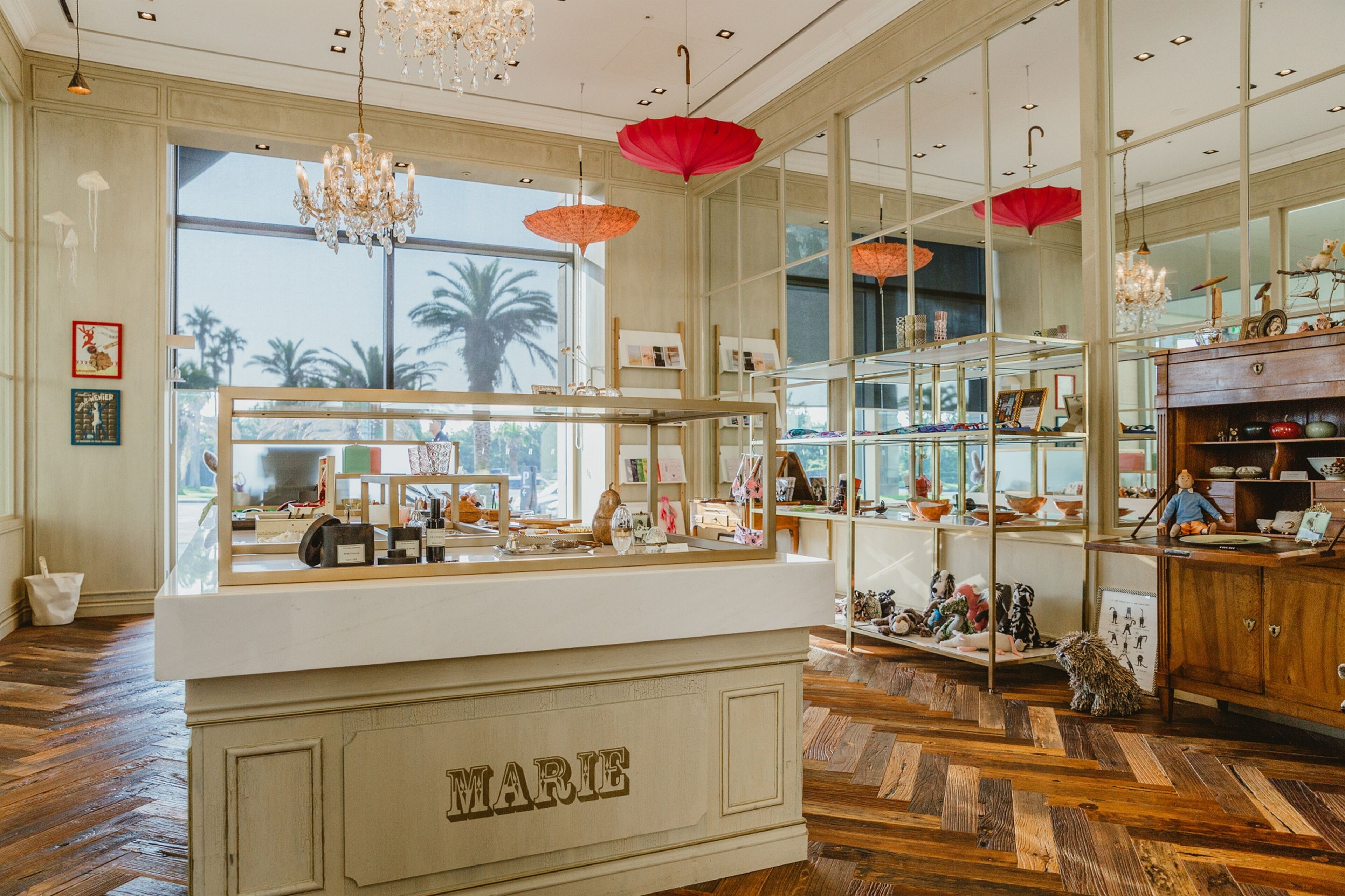 A boutique hotel interior with a central reception desk, wooden flooring, large windows with a view, and decorative red umbrellas.