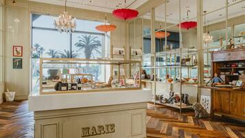 A boutique hotel interior with a central reception desk, wooden flooring, large windows with a view, and decorative red umbrellas.