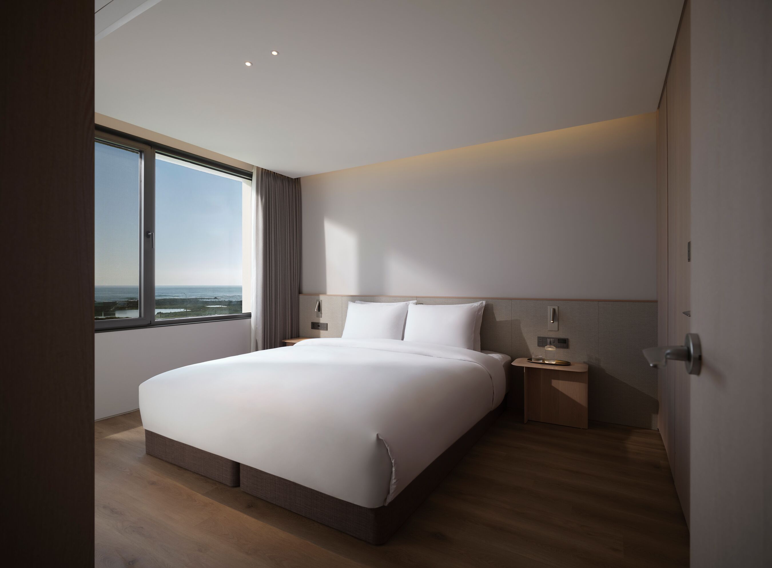 Une chambre d’hôtel moderne dotée d’un grand lit, d’une table de chevet et d’une commode, et offrant une vue sur l’océan.