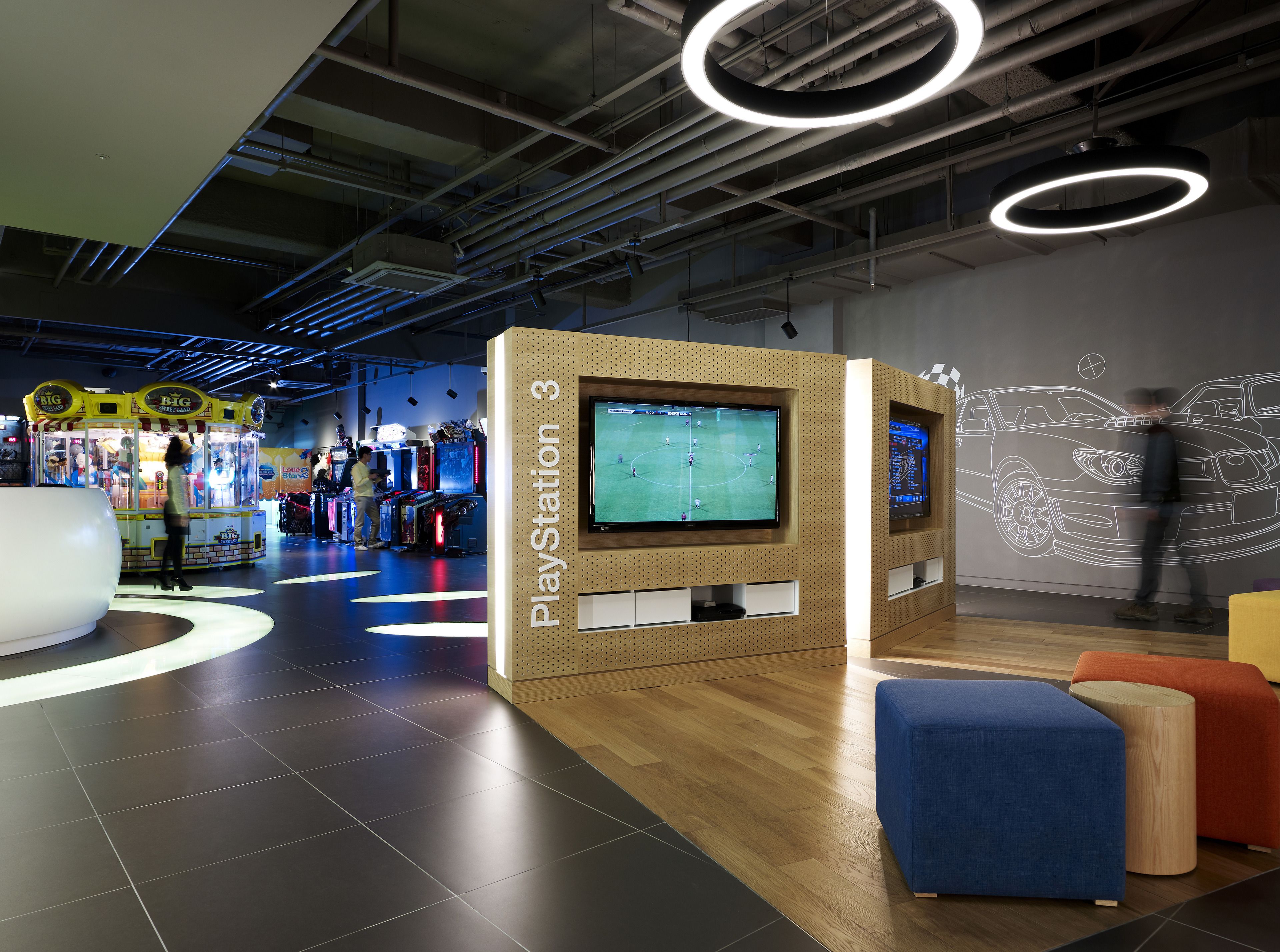 A PlayStation 3 gaming area with multiple screens, arcade games, and modern seating.